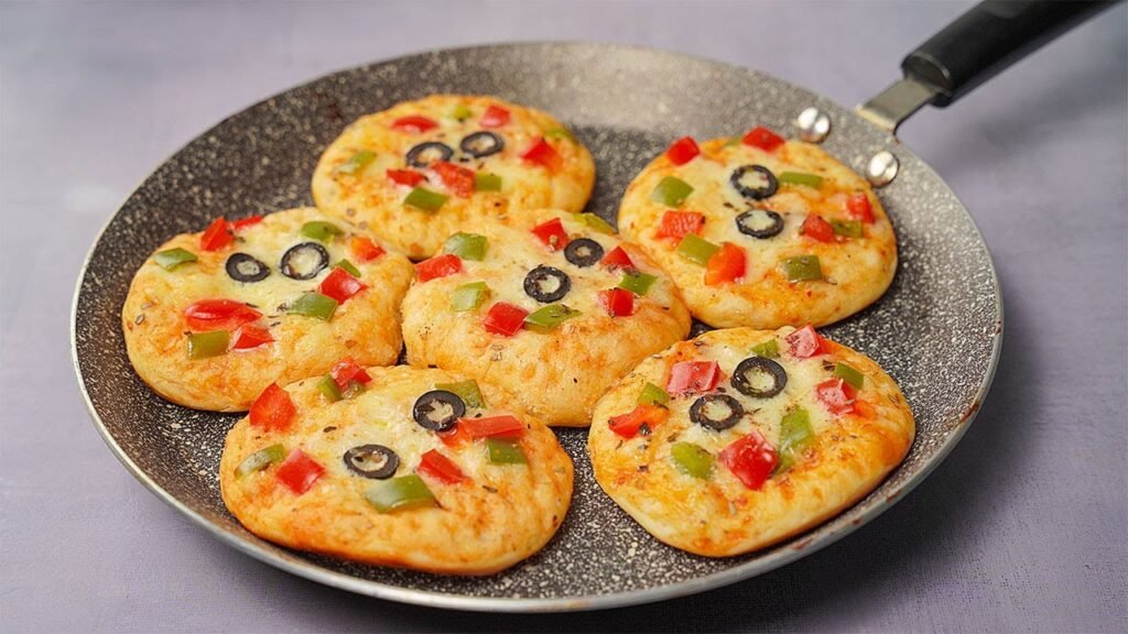 Mini pizzas topped with melted cheese, diced red and green peppers, and black olives in a skillet