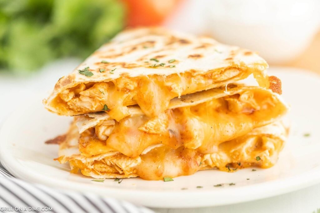 Stack of chicken and cheese quesadillas with melted cheese oozing out, garnished with fresh herbs