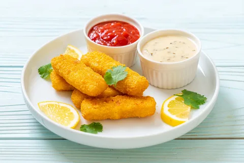 Crispy fish fingers with lemon slices and parsley, served with ketchup and creamy dipping sauce