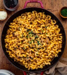 Pan of cavatappi pasta with sausage, herbs, and grated cheese beside small bowls of Parmesan and herbs