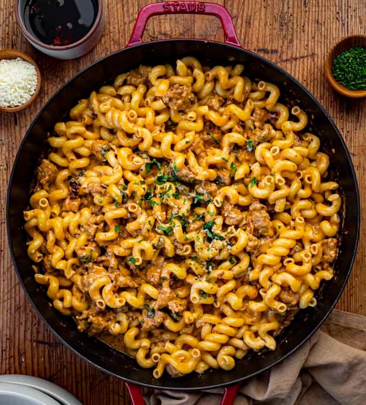 Skillet of creamy cavatappi pasta topped with fresh herbs and grated Parmesan on a rustic wooden table