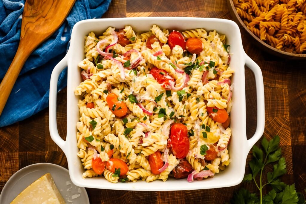 Overhead view of creamy baked Boursin pasta with fusilli, roasted cherry tomatoes, red onions, and fresh herbs in a white baking dish