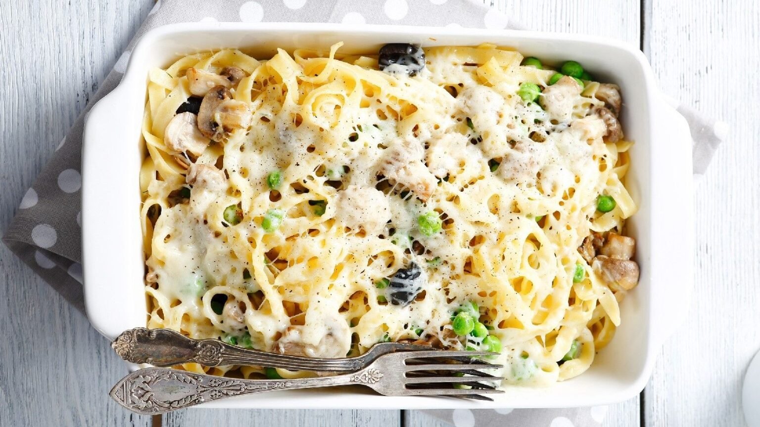 Baked creamy tagliatelle with mushrooms and peas in a white baking dish