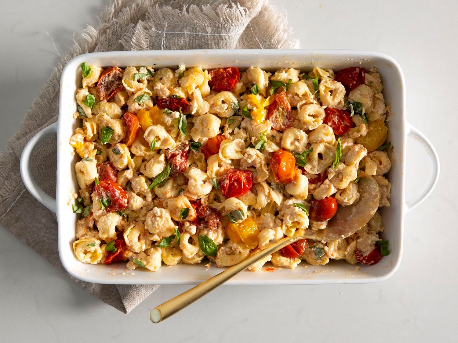 Creamy baked Boursin pasta with roasted cherry tomatoes and fresh basil in a white baking dish